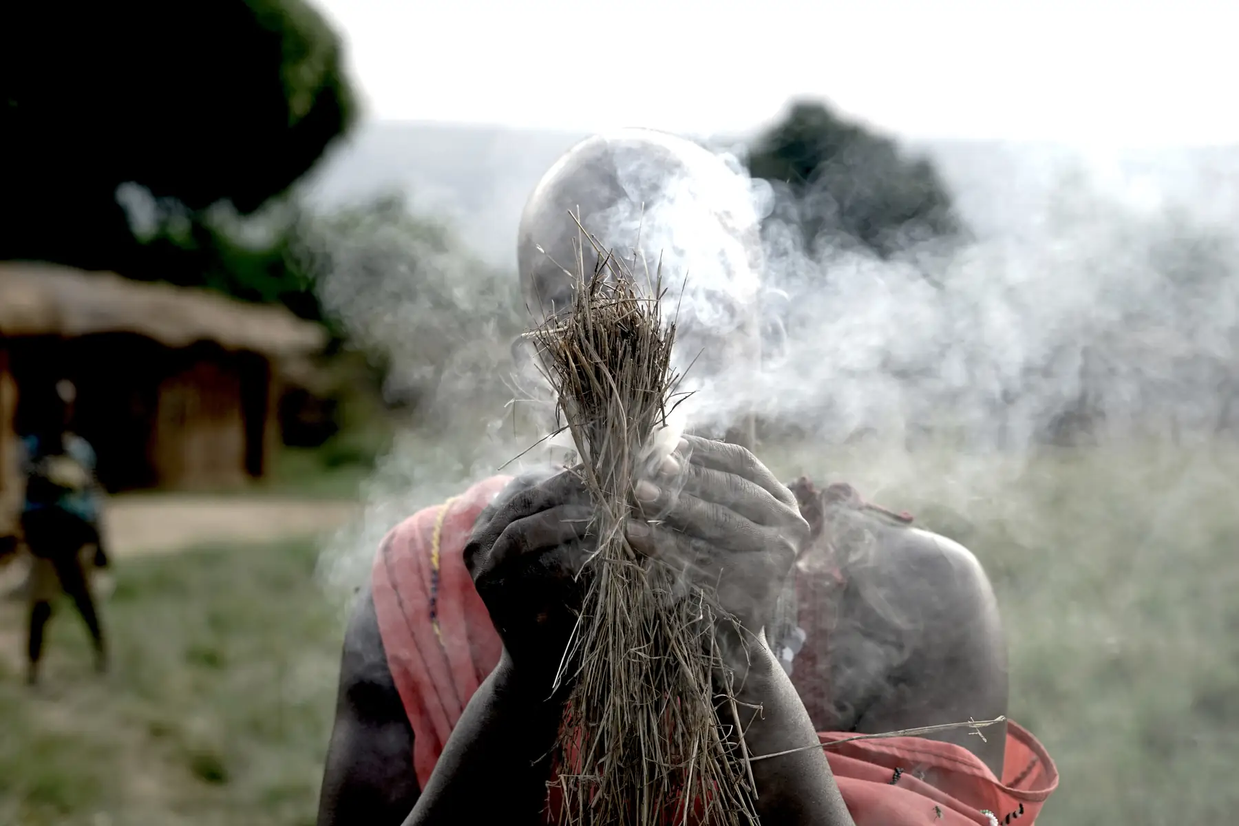 A Maasai man in red, wrapped in smoke
