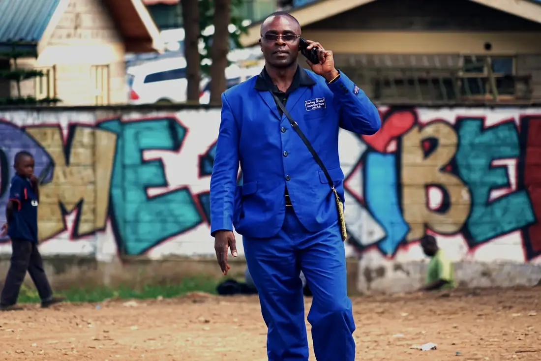 A man in blue overalls in front of a Kibera mural