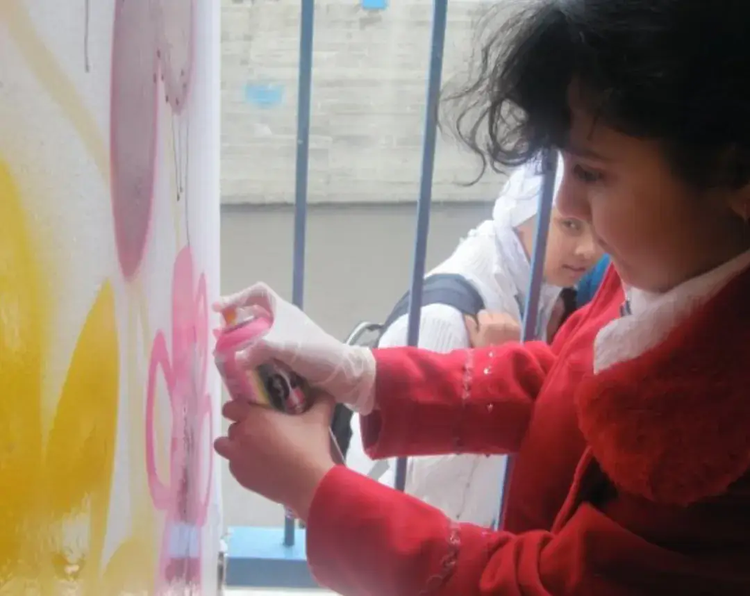 A girl in a red coat painting a wall during a workshop